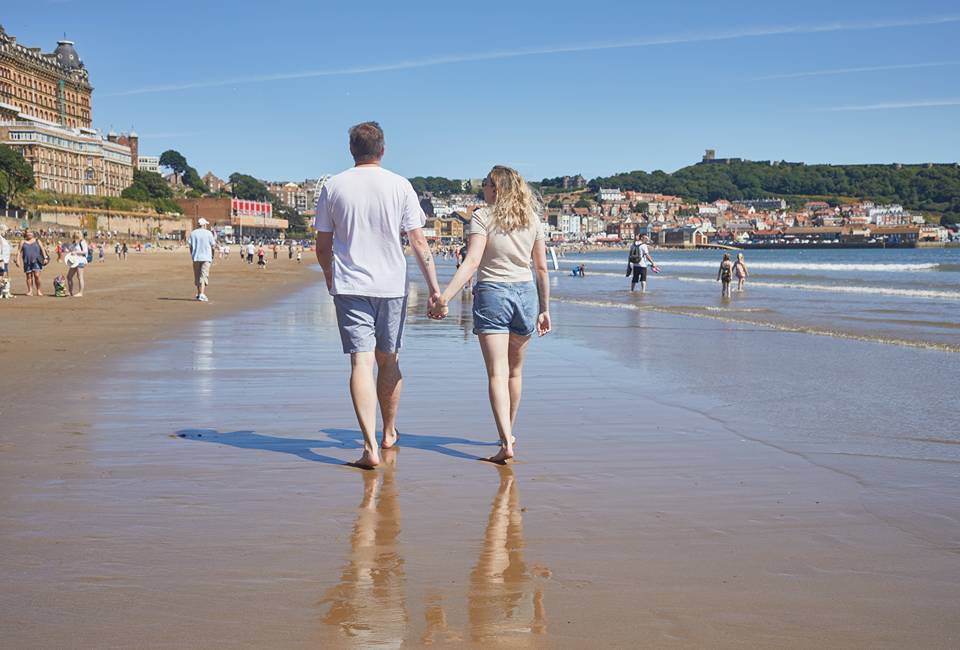 A couple walking hand-in-hand on a beach in Scarborough on a sunny day