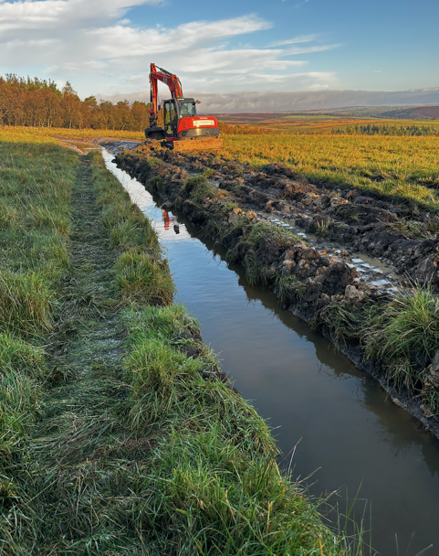 watercourse on farmland with digger in the background